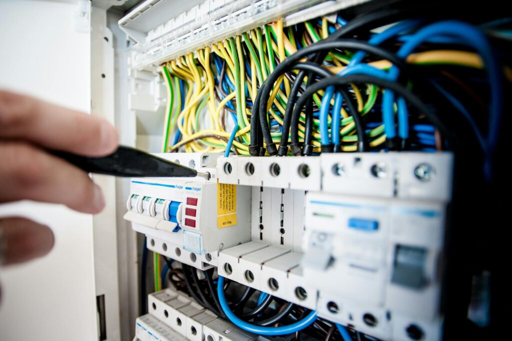 Hand of electrician working on a circuit breaker panel with colorful wires, ensuring safe electrical connections. Hand of electrician working on a circuit breaker panel with colorful wires, ensuring safe electrical connections.